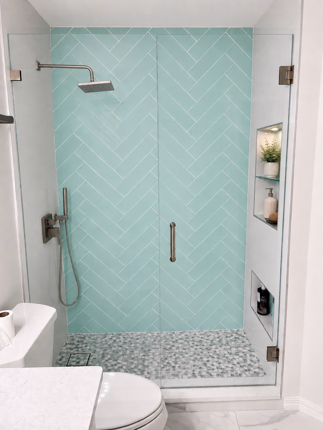 Walk-in shower with aqua herringbone tile, glass door and niche, remodeled by BFM Builders