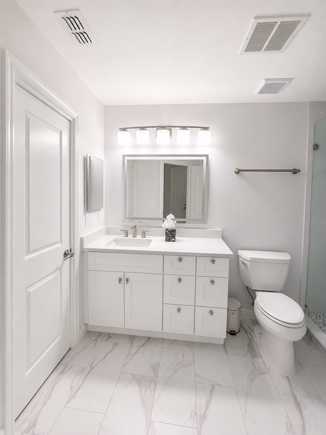 Guest bathroom with a white vanity, backlit mirror and marble-look floor tile, remodeled by BFM Builders