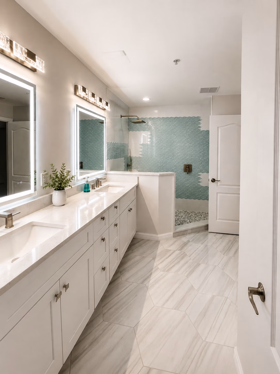 White double vanity with backlit mirrors facing an aqua glass tile shower, remodeled by BFM Builders
