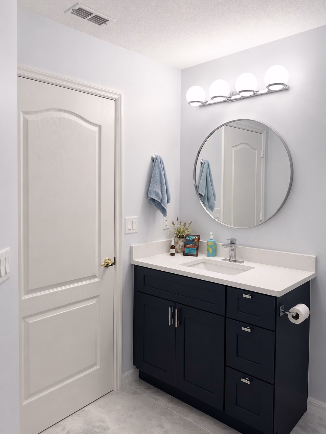 Navy vanity with a white countertop and round mirror in a guest bathroom remodeled by BFM Builders