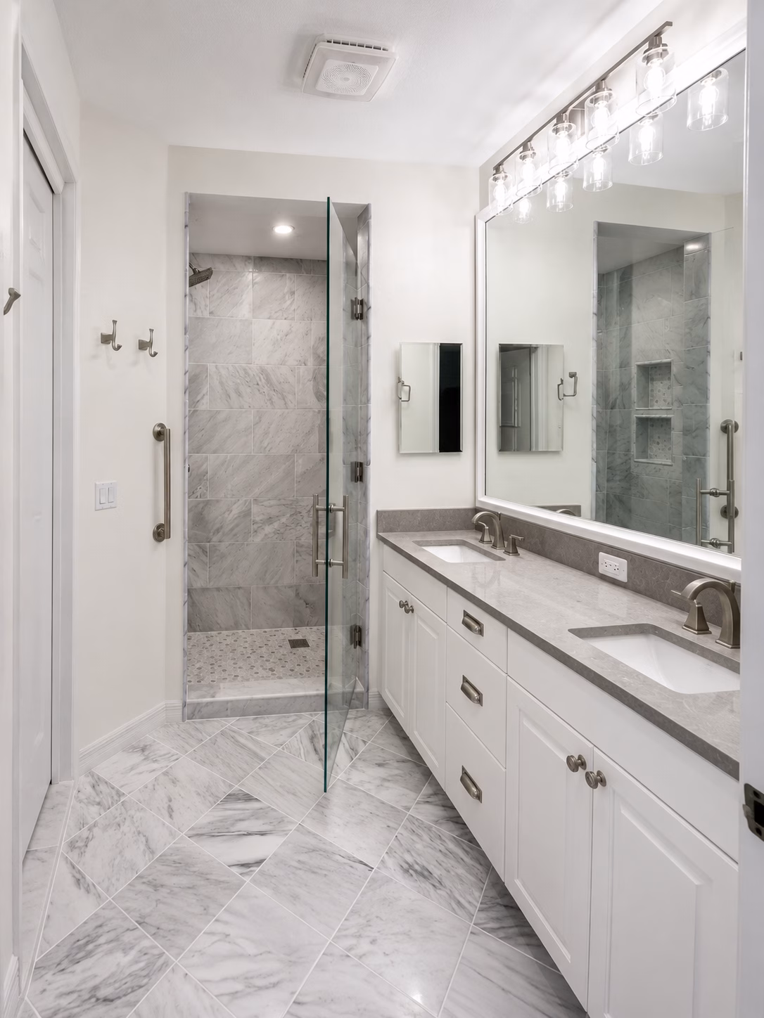 Frameless glass walk-in shower with two niches next to a double vanity, remodeled by BFM Builders